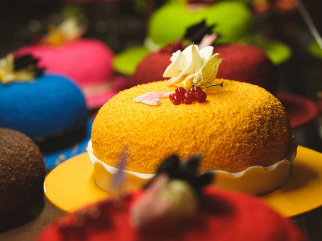 Vibrant display of assorted cakes adorned with fresh flowers and berries in a bakery.