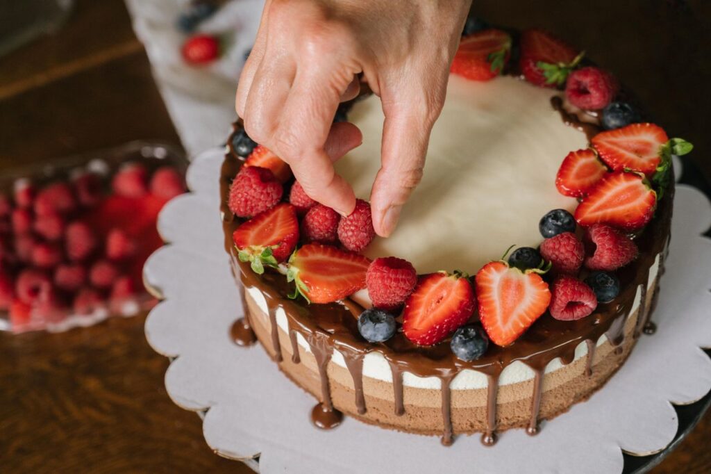 Hand placing fresh berries on a chocolate-covered cake, creating a delicious dessert.