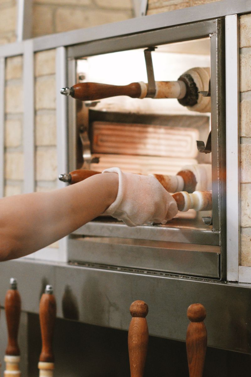 A female worker operates a traditional brick pizza oven in a pizzeria setting.